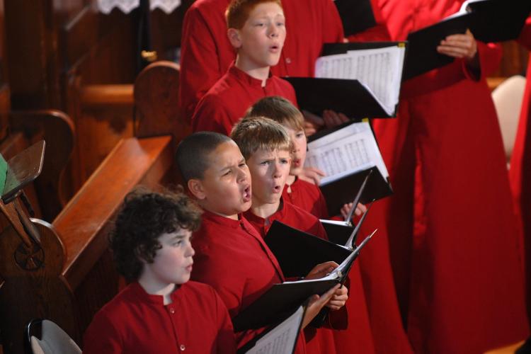 Boy choristers in red robes in a row, singing during concert